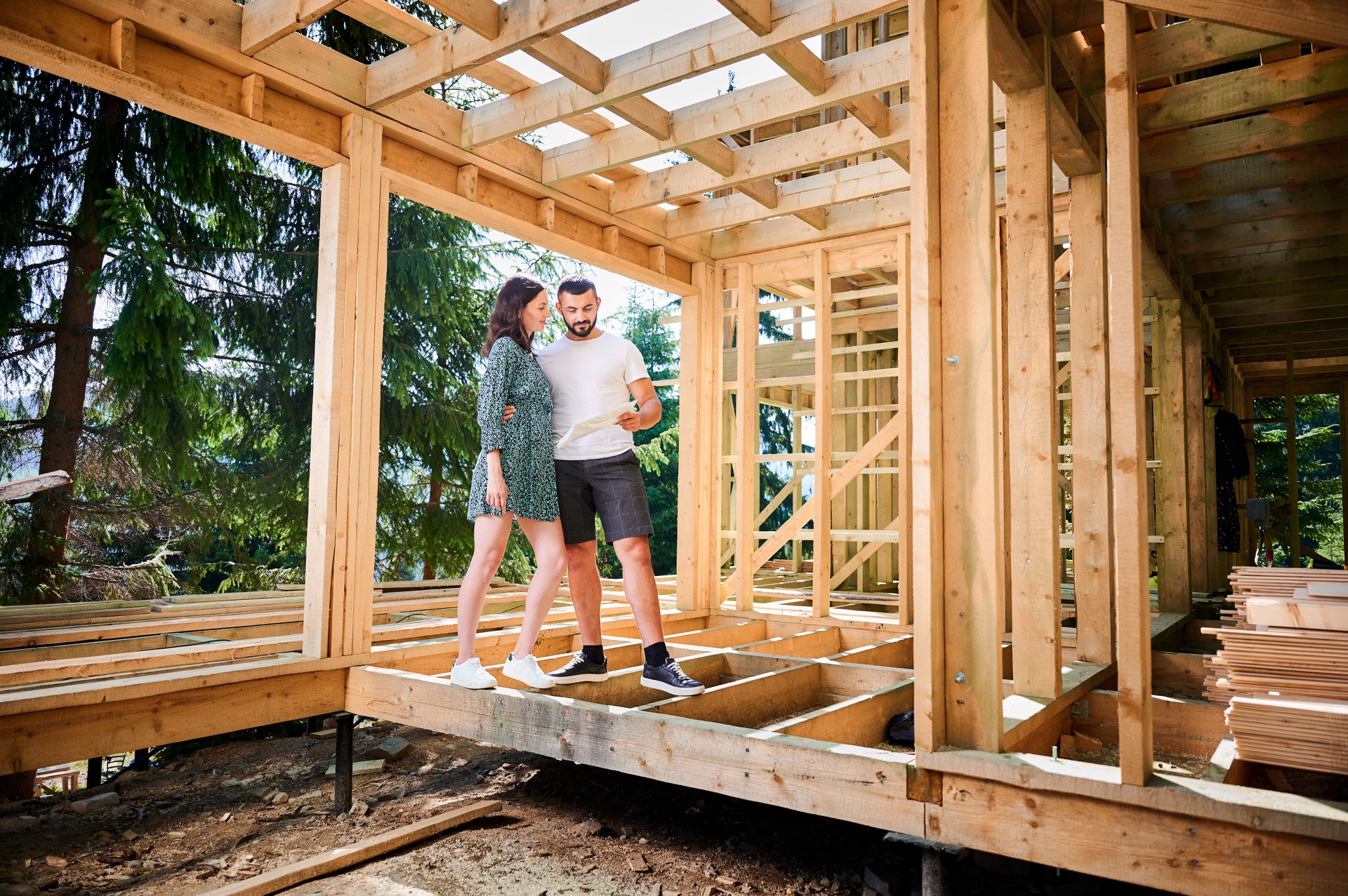 Man and woman inspecting their future wooden frame house nestled in the mountains near forest.